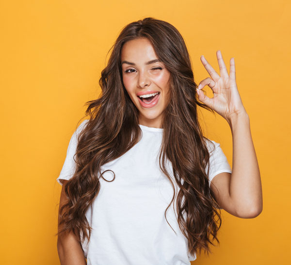 Girl winking and giving the okay sign against a yellow background