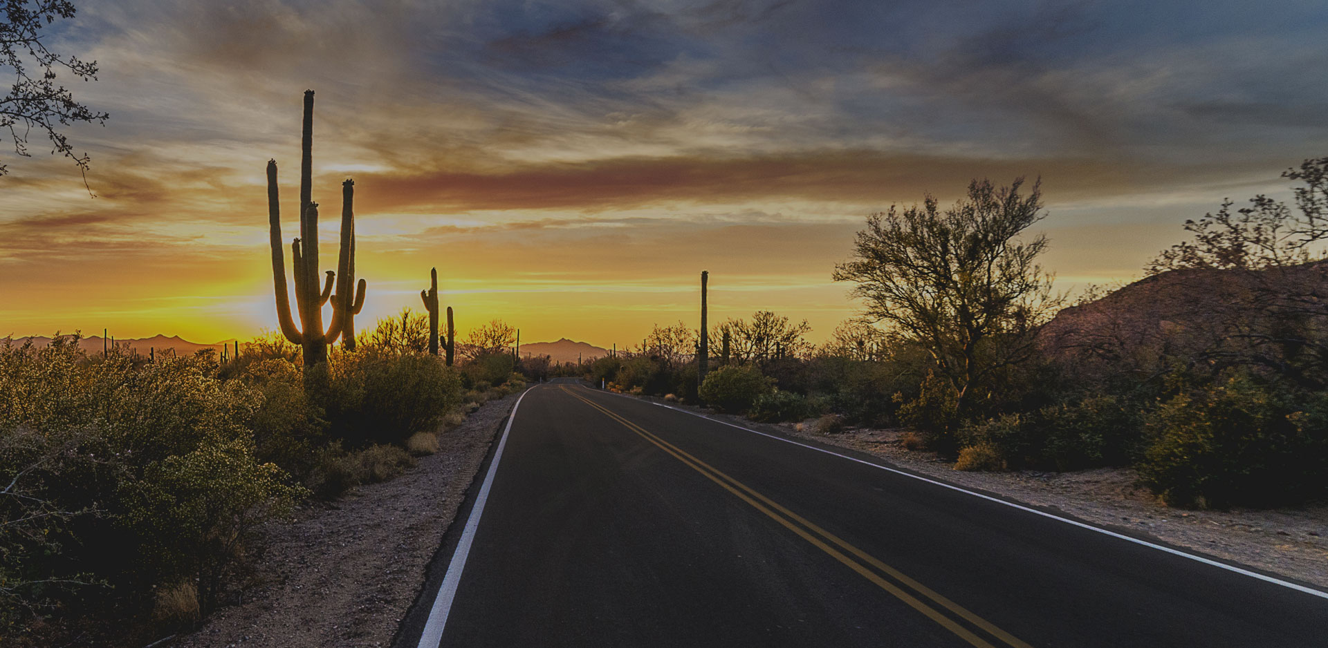 Road extends to the horizon, surrounded by Arizona desert, with sunset in the distance
